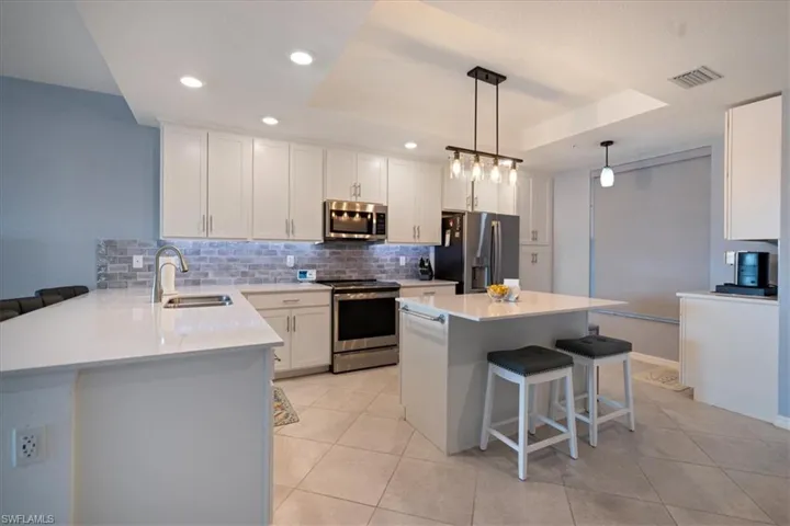 Kitchen featuring a breakfast bar area, a tray ceiling, stainless steel appliances, backsplash, and recessed lighting