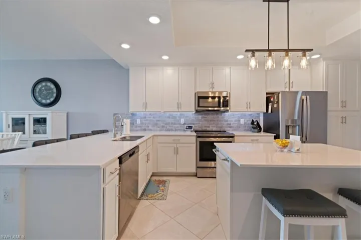 Kitchen with a kitchen bar, decorative backsplash, stainless steel appliances, recessed lighting, and white cabinets