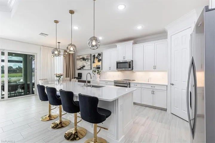 Kitchen featuring crown molding, stainless steel appliances, hanging light fixtures, a kitchen island with sink, and a breakfast bar