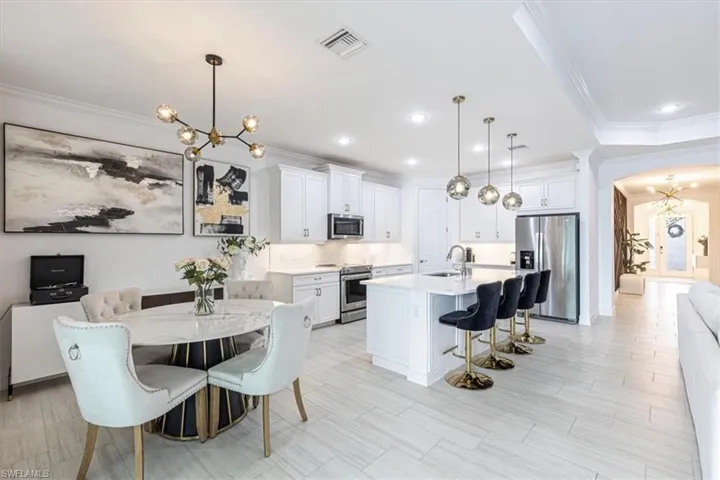 Kitchen featuring a chandelier, ornamental molding, a kitchen bar, stainless steel appliances, and white cabinetry