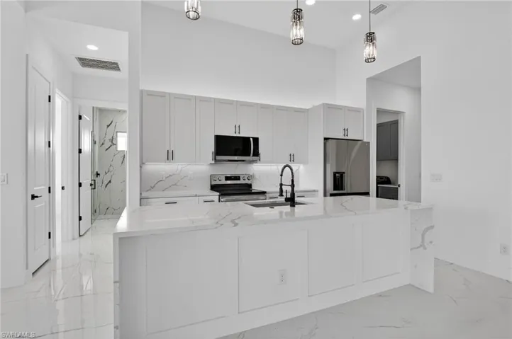Kitchen with light stone counters, stainless steel appliances, light marble finish flooring, white cabinets, and a spacious island