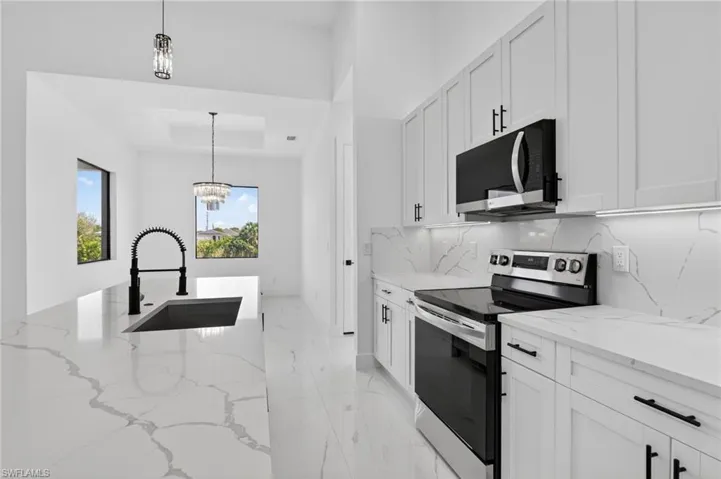Kitchen featuring stainless steel electric stove, light stone counters, a raised ceiling, a chandelier, and white cabinets