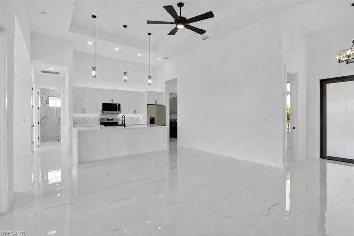 Unfurnished living room with light marble finish flooring, a raised ceiling, a ceiling fan, healthy amount of natural light, and recessed lighting