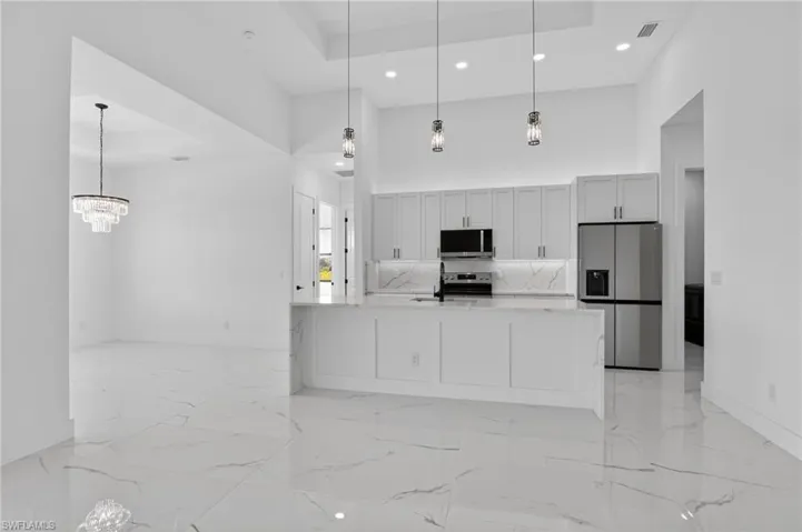 Kitchen featuring stainless steel appliances, a high tray ceiling, light stone countertops, a large island with sink, and light marble finish flooring