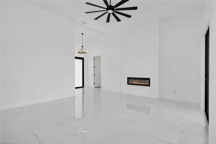 Living room featuring a high ceiling, a glass covered fireplace, light marble finish floors, and a ceiling fan