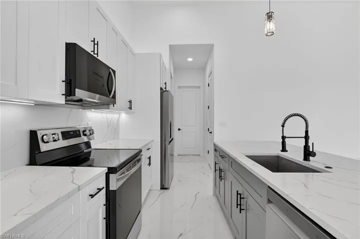 Kitchen with stainless steel appliances, light stone countertops, hanging light fixtures, white cabinets, and light marble finish floors
