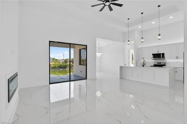Unfurnished living room featuring a tray ceiling, ceiling fan, a glass covered fireplace, and recessed lighting
