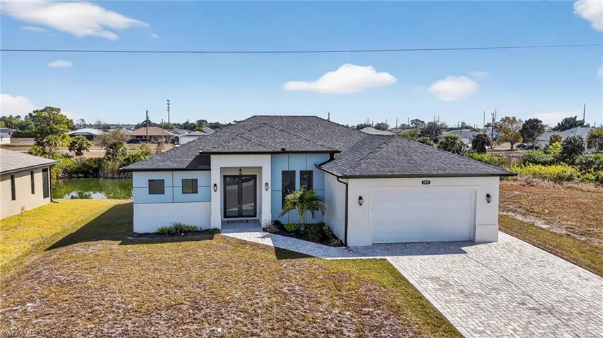 View of front facade featuring a shingled roof, stucco siding, decorative driveway, a front lawn, and an attached garage