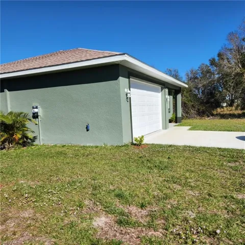 View of property exterior with stucco siding, a lawn, driveway, and roof with shingles