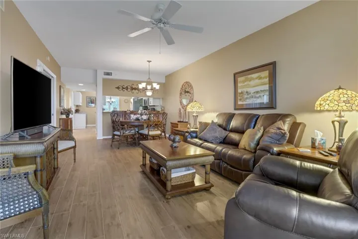Living room with light wood-type flooring and ceiling fan with notable chandelier