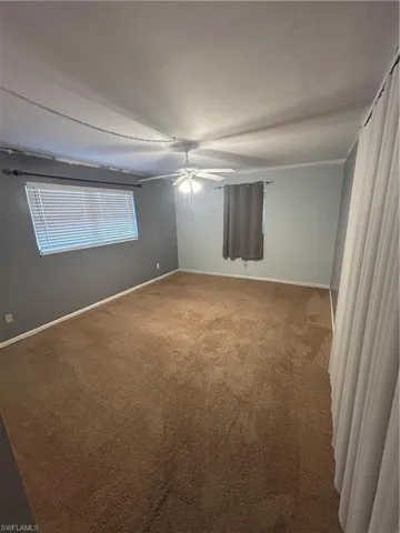 Carpeted empty room with ceiling fan and baseboards