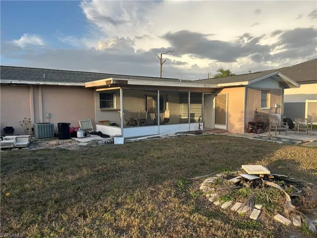 Back of house featuring a lawn, a sunroom, stucco siding, a patio, and roof with shingles