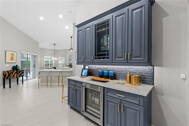 Kitchen with decorative backsplash, a kitchen breakfast bar, lofted ceiling, wine cooler, and pendant lighting