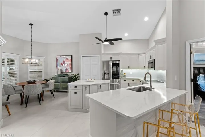 Kitchen with white cabinets, stainless steel appliances, sink, high vaulted ceiling, and a center island with sink
