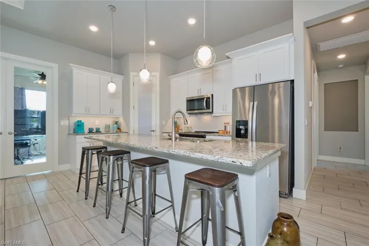 Kitchen featuring white cabinetry, sink, appliances with stainless steel finishes, an island with sink, and pendant lighting