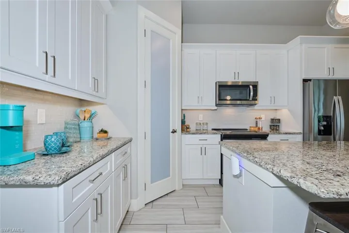 Kitchen with stainless steel appliances, white cabinets, light granite counters, and decorative backsplash