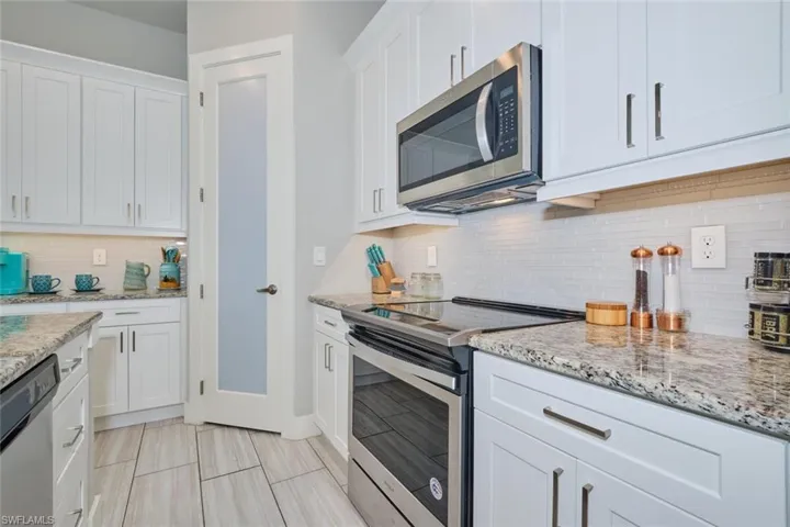 Kitchen featuring tasteful backsplash, light granite countertops, white cabinets, and stainless steel appliances