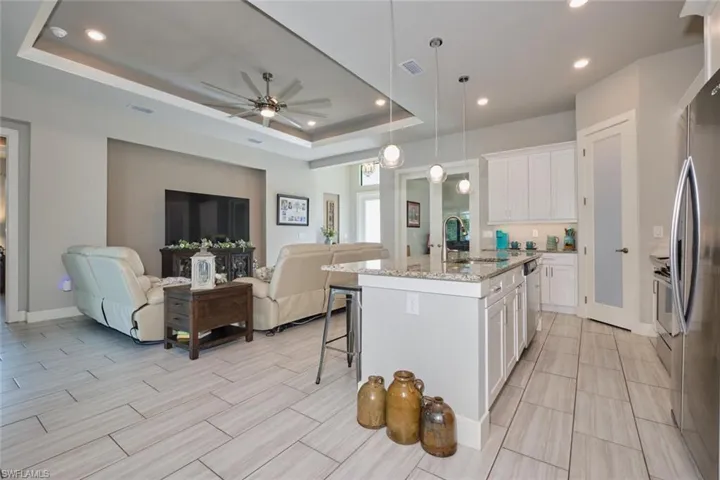 Kitchen with a center island with sink, sink, a tray ceiling, white cabinetry, and decorative light fixtures