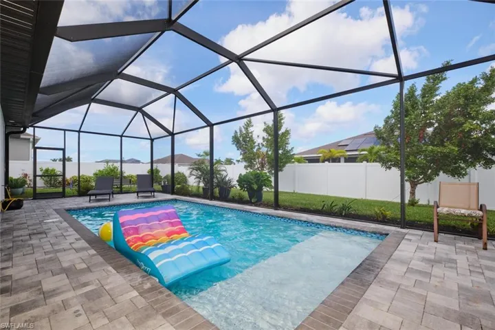 View of swimming pool with sun shelf and bubbler, glass enclosure, and a patio area