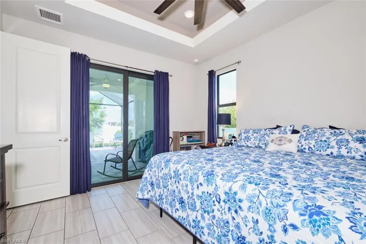 Primary Bedroom with access to outside, multiple windows, ceiling fan, and tray ceiling