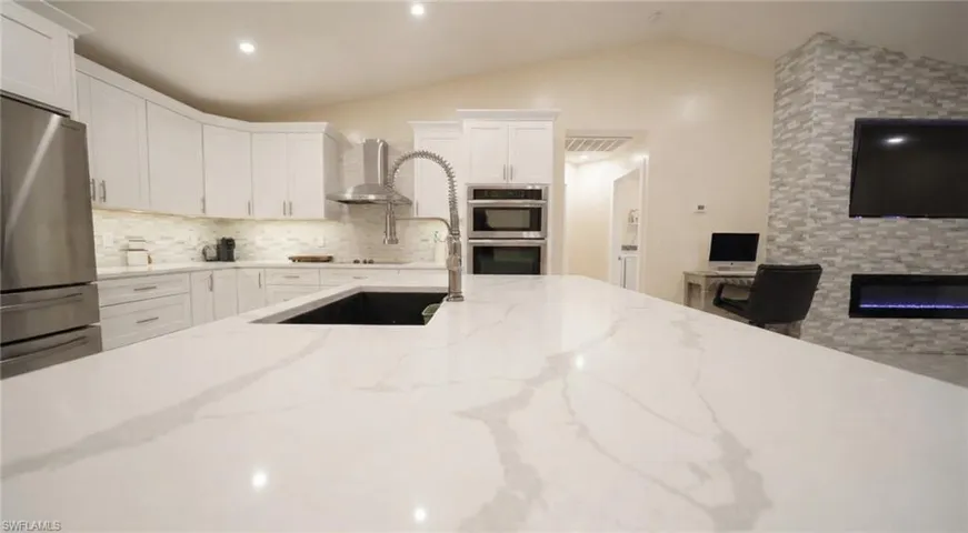 Kitchen featuring white cabinets, appliances with stainless steel finishes, light stone countertops, wall chimney exhaust hood, and tasteful backsplash