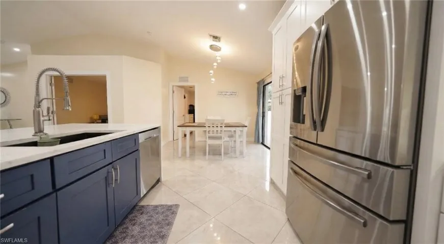 Kitchen featuring stainless steel appliances, vaulted ceiling, light stone countertops, blue cabinetry, and light tile patterned floors
