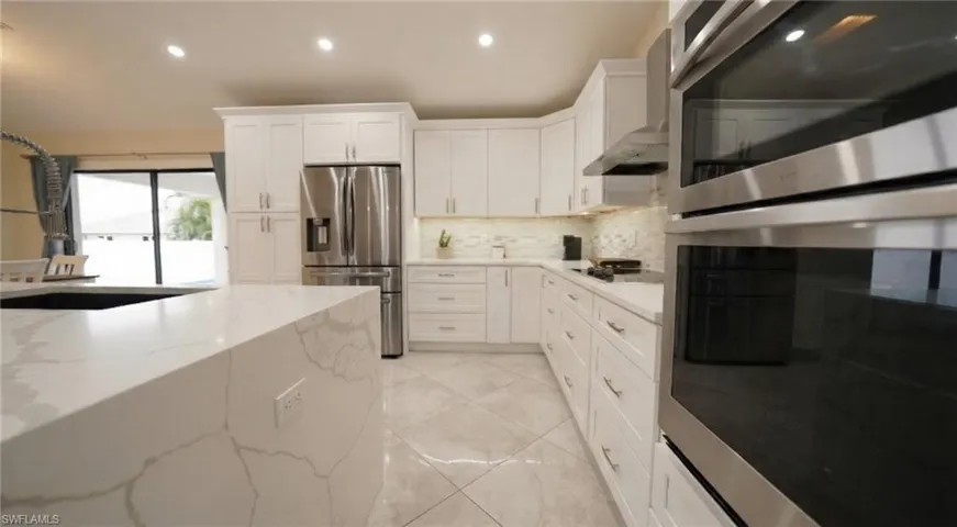 Kitchen featuring stainless steel appliances, white cabinets, recessed lighting, wall chimney exhaust hood, and light stone countertops