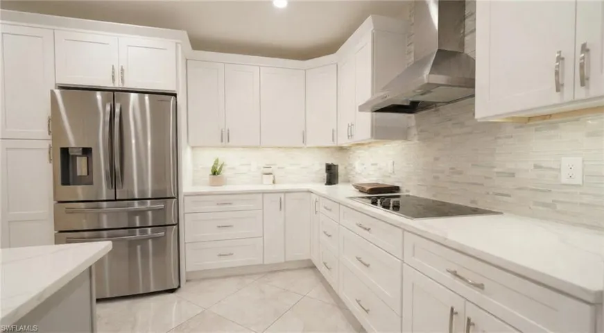 Kitchen featuring stainless steel fridge with ice dispenser, wall chimney range hood, white cabinetry, tasteful backsplash, and light stone countertops