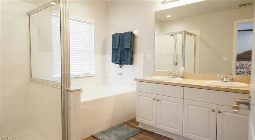 Full bathroom with a stall shower, a bath, double vanity, and dark wood finished floors