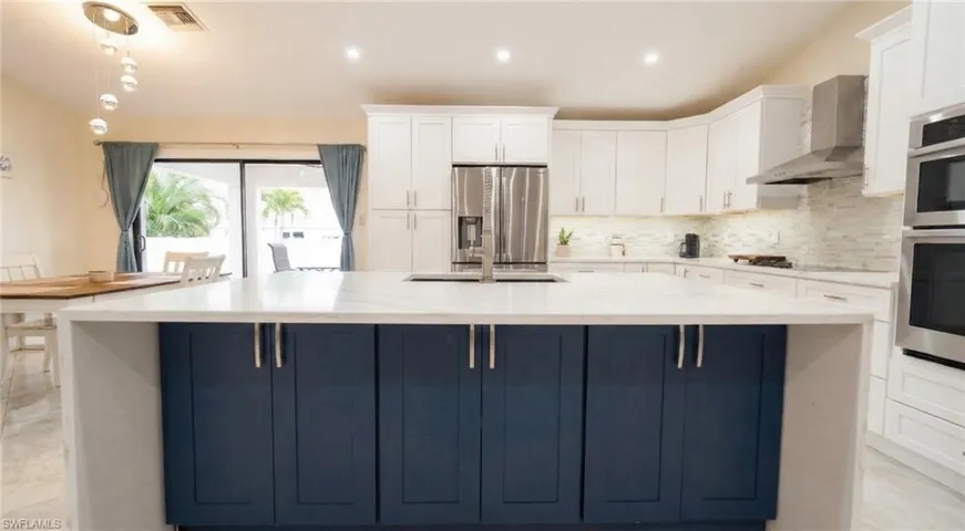Kitchen featuring white cabinets, stainless steel appliances, wall chimney range hood, light stone counters, and a spacious island
