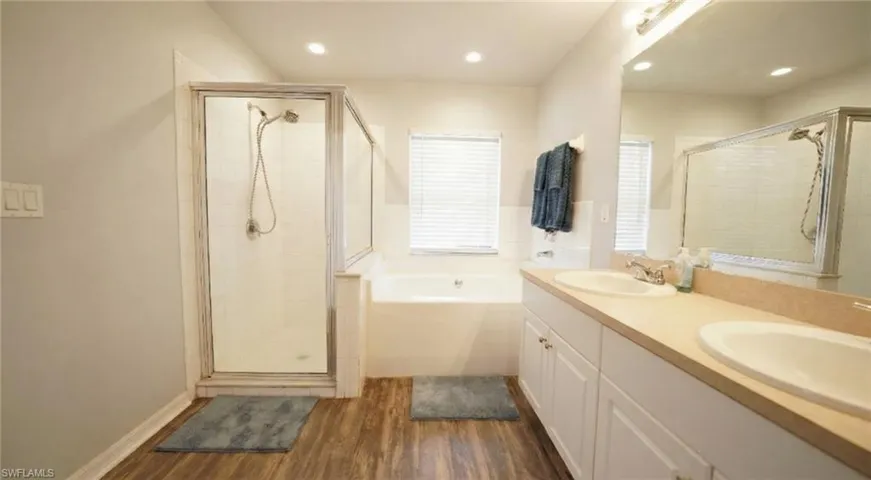 Full bath featuring a garden tub, a shower stall, double vanity, and dark wood-type flooring