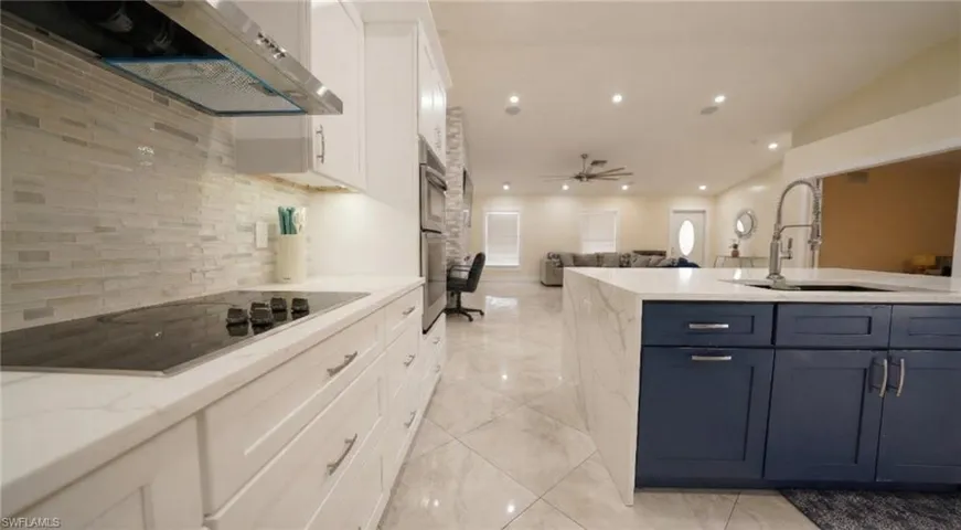 Kitchen featuring open floor plan, light stone counters, ventilation hood, black electric stovetop, and backsplash