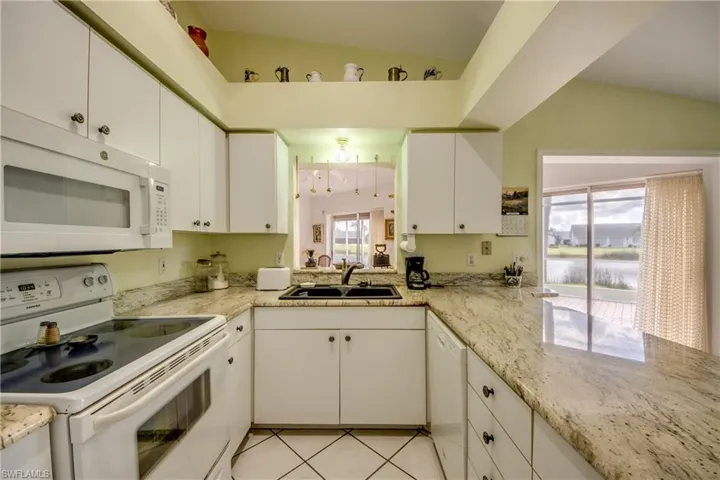 Kitchen with white cabinetry, lofted ceiling, white appliances, Granite counter-tops, and light tile floors