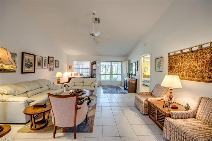 Tiled living room featuring high vaulted ceiling and ceiling fan.  Looking to double door entry.