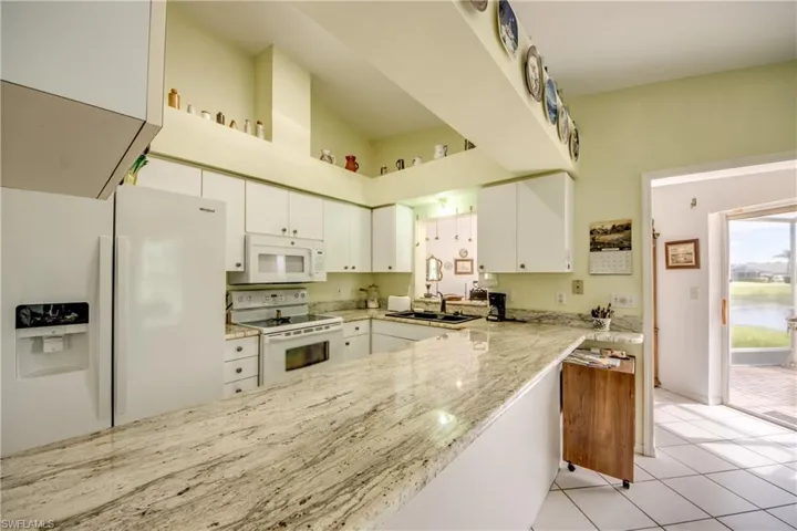 Kitchen with white appliances, white cabinets, light stone counters, a towering ceiling, and light tile flooring