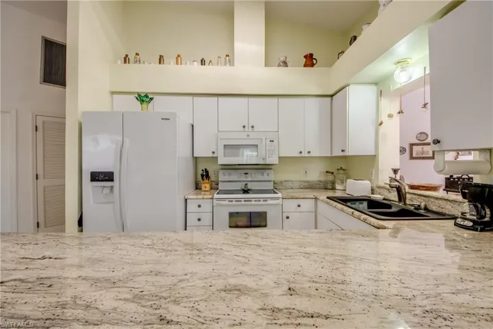 Kitchen with white appliances, white cabinets, kitchen peninsula, high vaulted ceiling, and sink