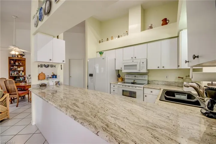Kitchen with white appliances, light tile floors, a high ceiling, sink, white cabinetry and Granite tops.