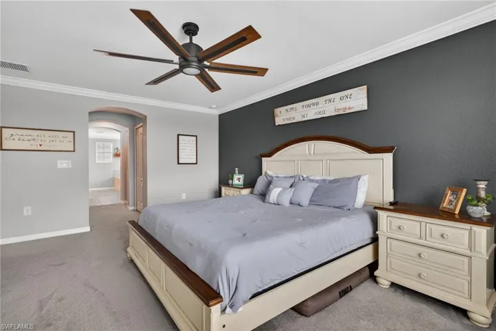 Bedroom with light colored carpet, ornamental molding, arched walkways, ceiling fan, and connected bathroom