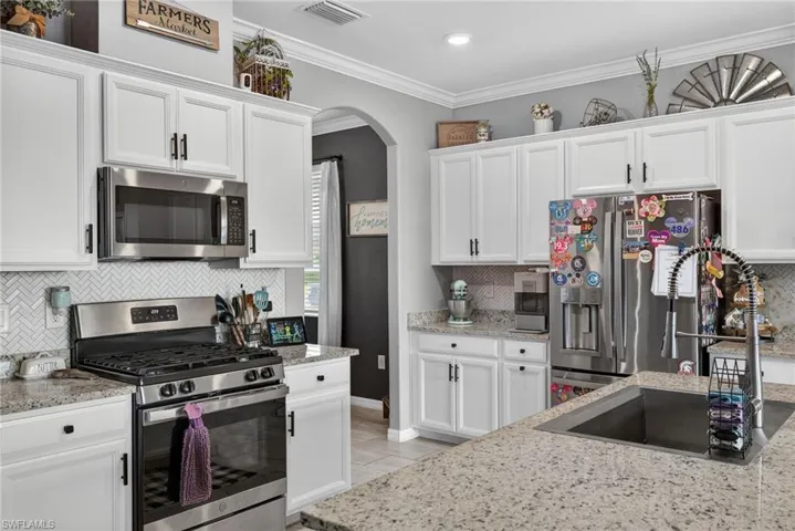 Kitchen with appliances with stainless steel finishes, ornamental molding, white cabinets, tasteful backsplash, and arched walkways