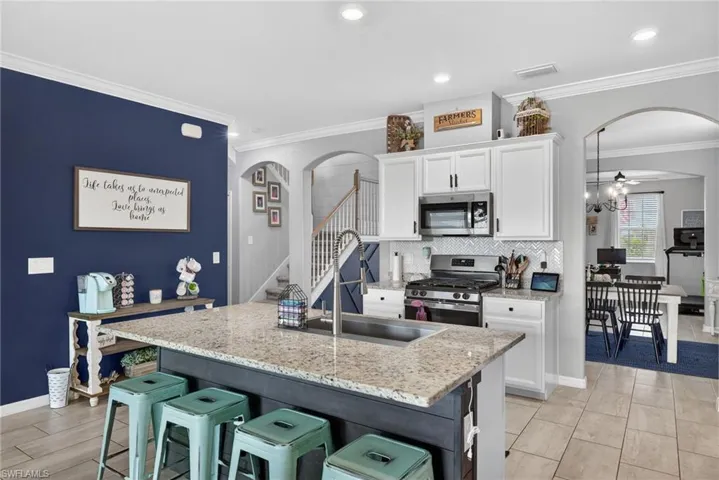 Kitchen with arched walkways, appliances with stainless steel finishes, a kitchen bar, light stone countertops, and ornamental molding