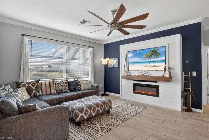 Living area featuring wood finish floors, crown molding, a glass covered fireplace, and ceiling fan