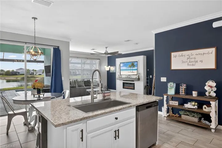 Kitchen with white cabinetry, light stone countertops, hanging light fixtures, a center island with sink, and stainless steel dishwasher