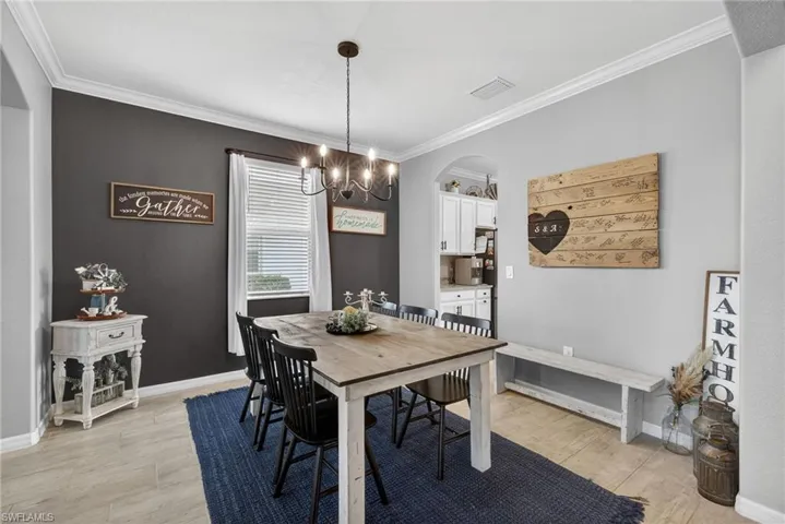Dining area with crown molding, light wood-style floors, a chandelier, and arched walkways