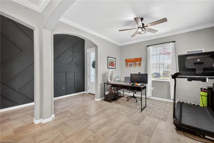 Office with crown molding, arched walkways, wood finish floors, and a ceiling fan