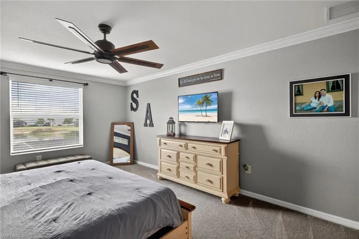 Bedroom featuring ornamental molding, light carpet, a ceiling fan, and a textured wall