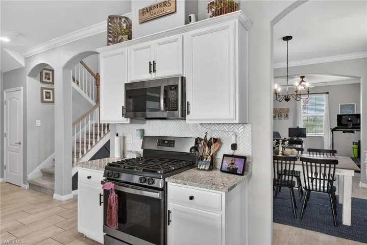 Kitchen with ornamental molding, arched walkways, stainless steel appliances, white cabinetry, and light stone counters