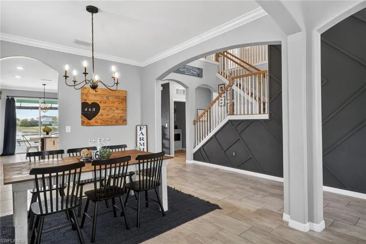 Dining room with crown molding, arched walkways, light wood-style floors, stairs, and a chandelier