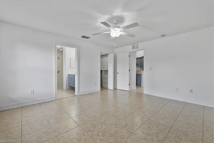 Unfurnished bedroom with ensuite bath, light tile patterned floors, a spacious closet, and a ceiling fan