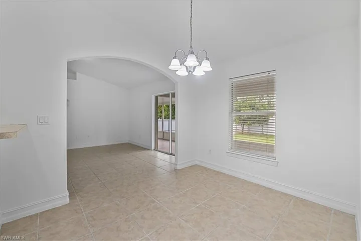 Empty room featuring arched walkways, a chandelier, light tile patterned floors, and vaulted ceiling