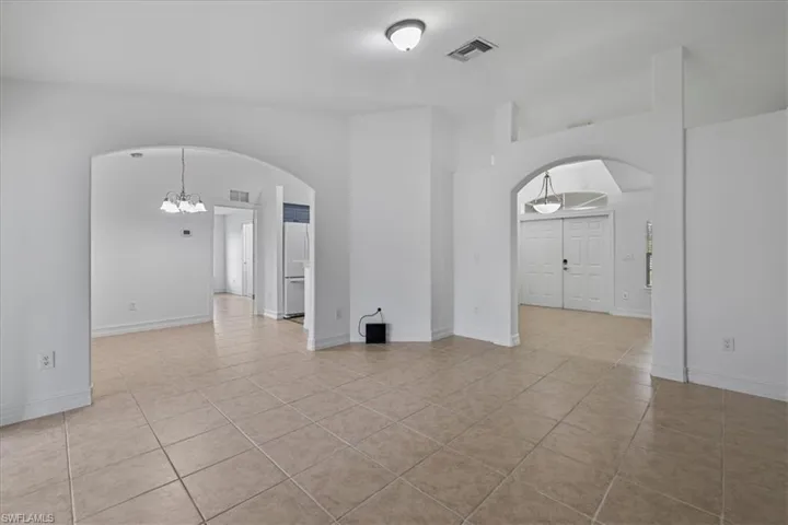 Spare room featuring arched walkways, light tile patterned flooring, and a chandelier